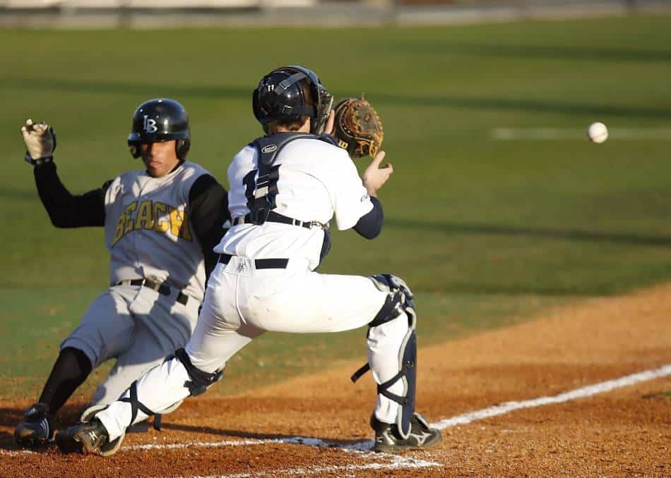 Runner in baseball tries to score by sliding home past catcher.