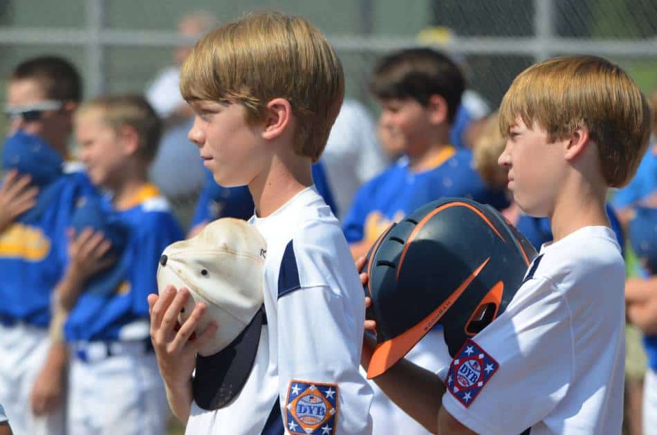 Youth baseball players take off their hats and helmets for the national anthem.