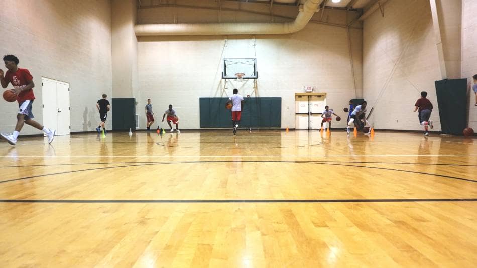 Basketball team going through dribbling drills inside a gym.