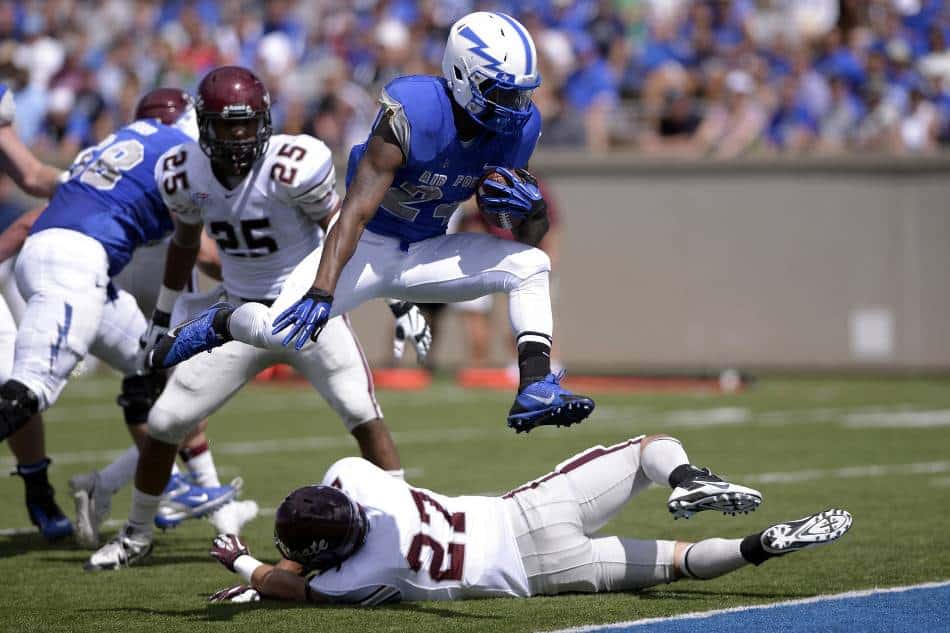 College football player jumps over defender to score touchdown.