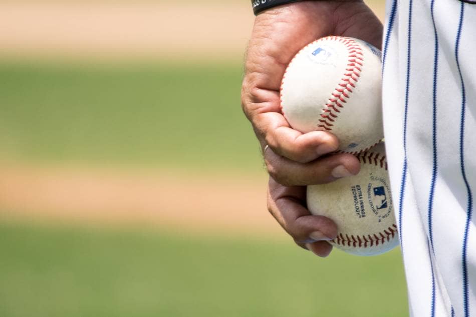 Baseball coach holding two baseballs, while coaching a base.