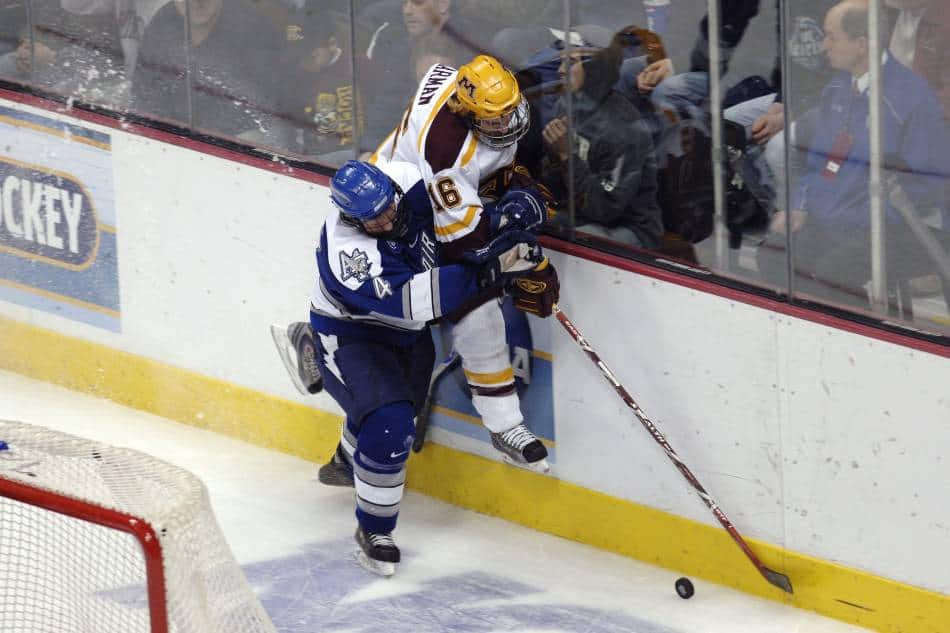 College hockey players battle for puck along the boards.