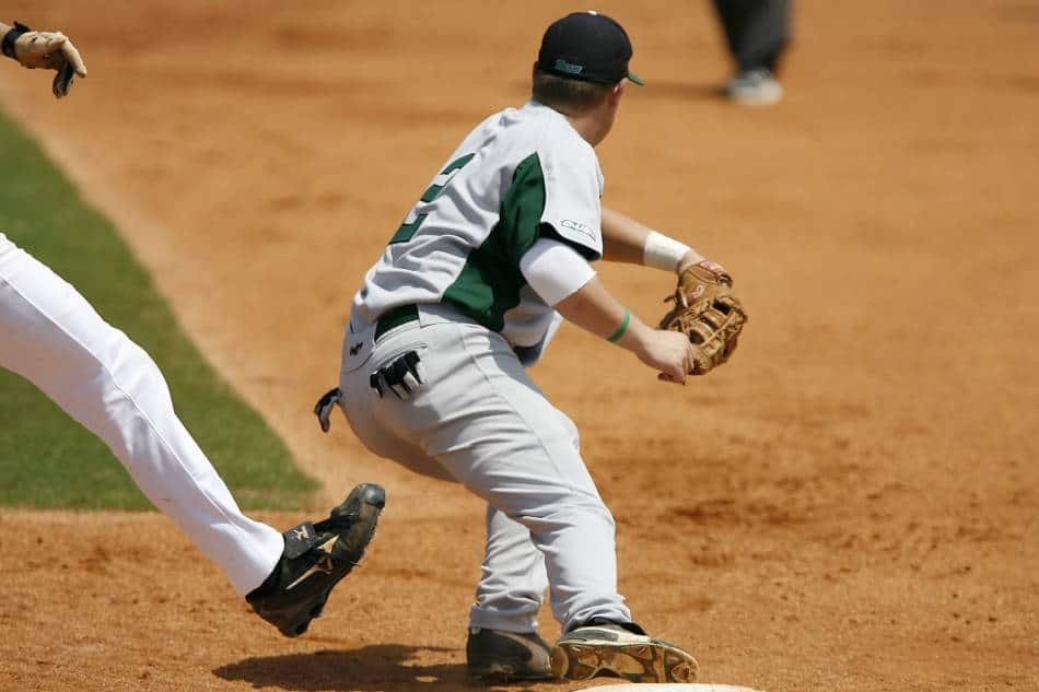 First baseman in grey and green prepares to catch the throw to get the runner out.