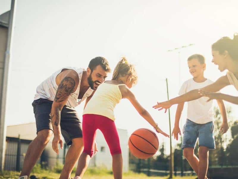 Young girl dribbling basketball with family.