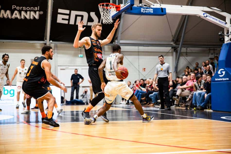 Basketball player in black tries to guard player in white without fouling him.