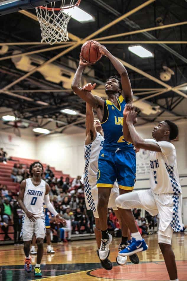 Basketball player in blue and gold fouled during shooting by player in white.