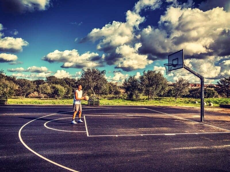 Man in white tank top shooting free throws at the park.