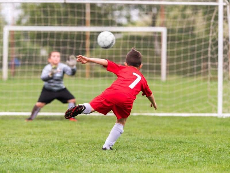 jucător de fotbal de tineret în tricou roșu șutează mingea de fotbal la net.