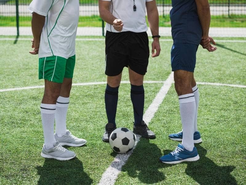 Soccer referee flips coin in front of two players.