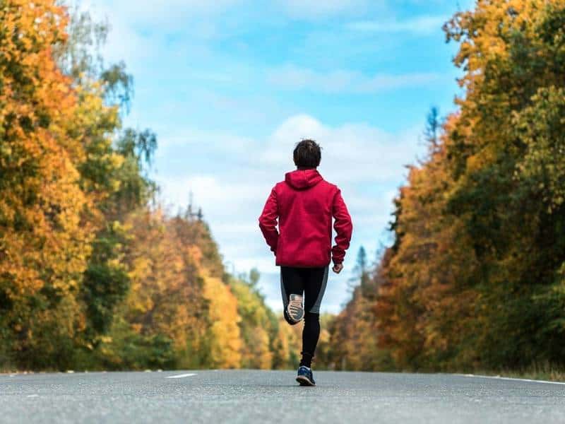 Man in red hoodie runs on a paved road.