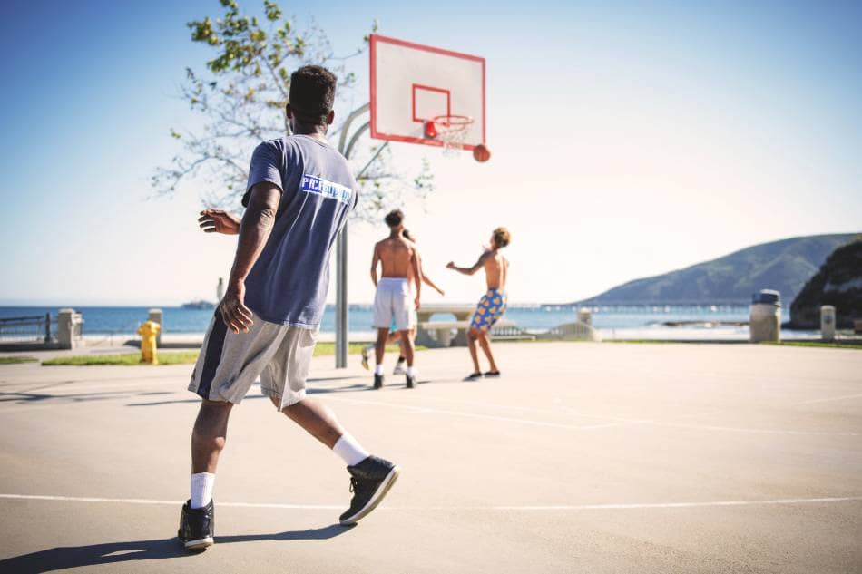 Four men playing basketball near the ocean.