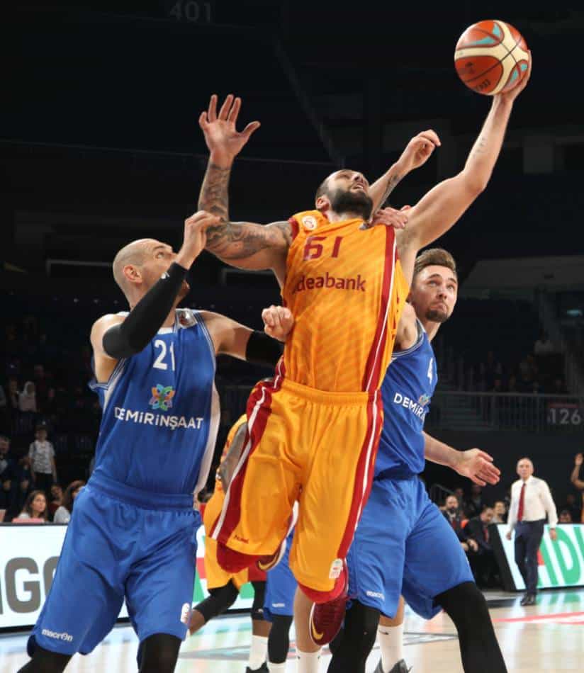 Basketball players in blue jerseys foul player in orange and red jersey.