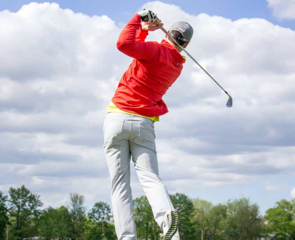 Golfer in red watches a shot he took with his iron.