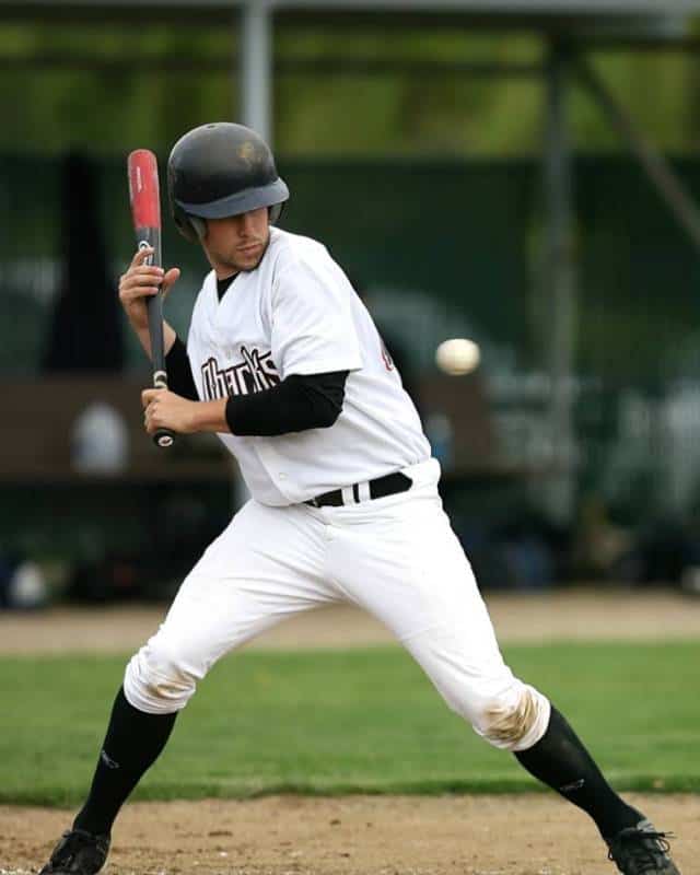 Baseball batter in white braces himself to get hit by a pitch.