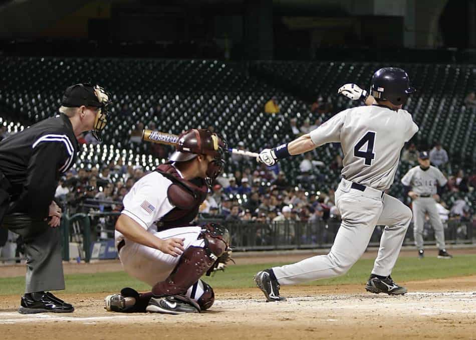 College baseball player puts the ball in play as the catcher and umpire look on.