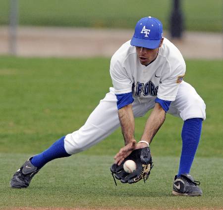 A college baseball player fields a groundball just outside the infield.