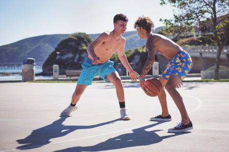 Two basketball players playing basketball outside near the ocean.