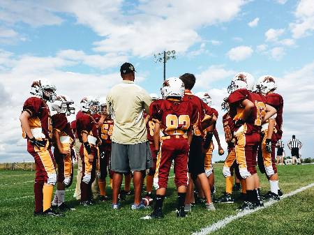 A coach huddles around with his youth football team.