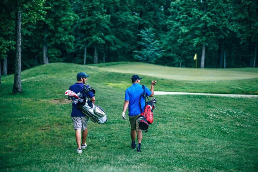 Two golfers walk toward the green to putt their balls.