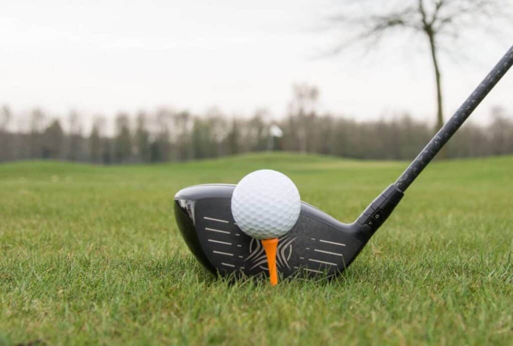 A golfer lines up their driver behind a tee'd up ball.