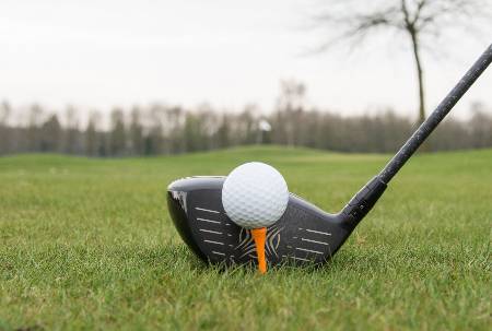 A golfer lines up their driver behind a tee'd up ball.