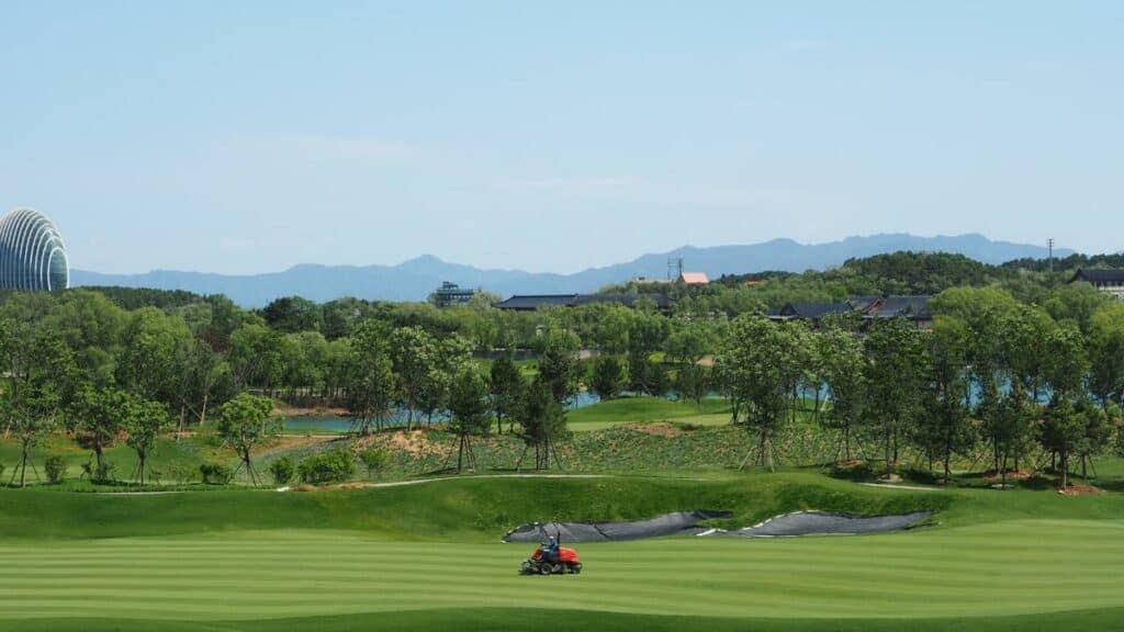 A groundskeeper mowing the fairway on a golf course.