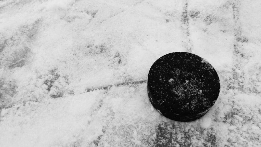 A hockey puck sits on a sheet of ice.