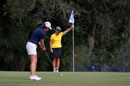 A female golfer in blue putts the ball.