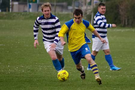 A soccer player in yellow and blue dribbles past a defender.