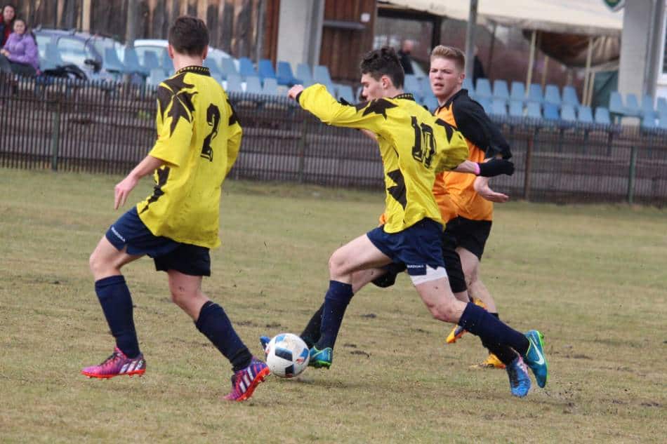 A soccer player in yellow tries to protect the ball from the team in orange.