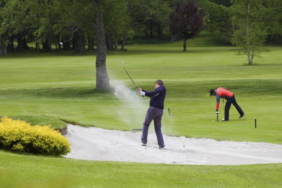 A golfer takes a shot out of a bunker.