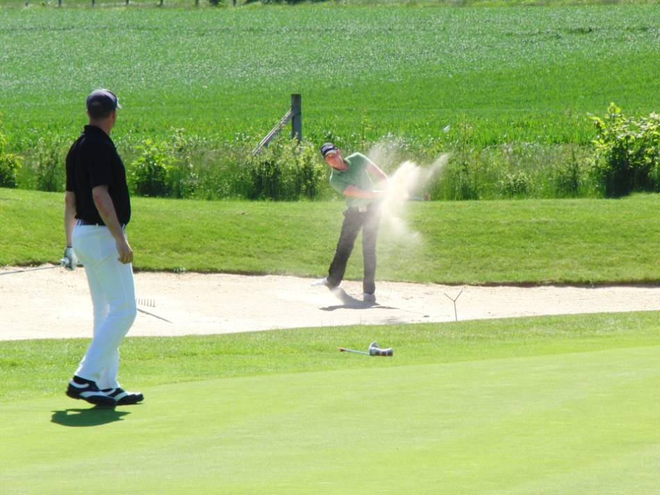 A golfer takes a swing with his sand wedge out of a bunker.