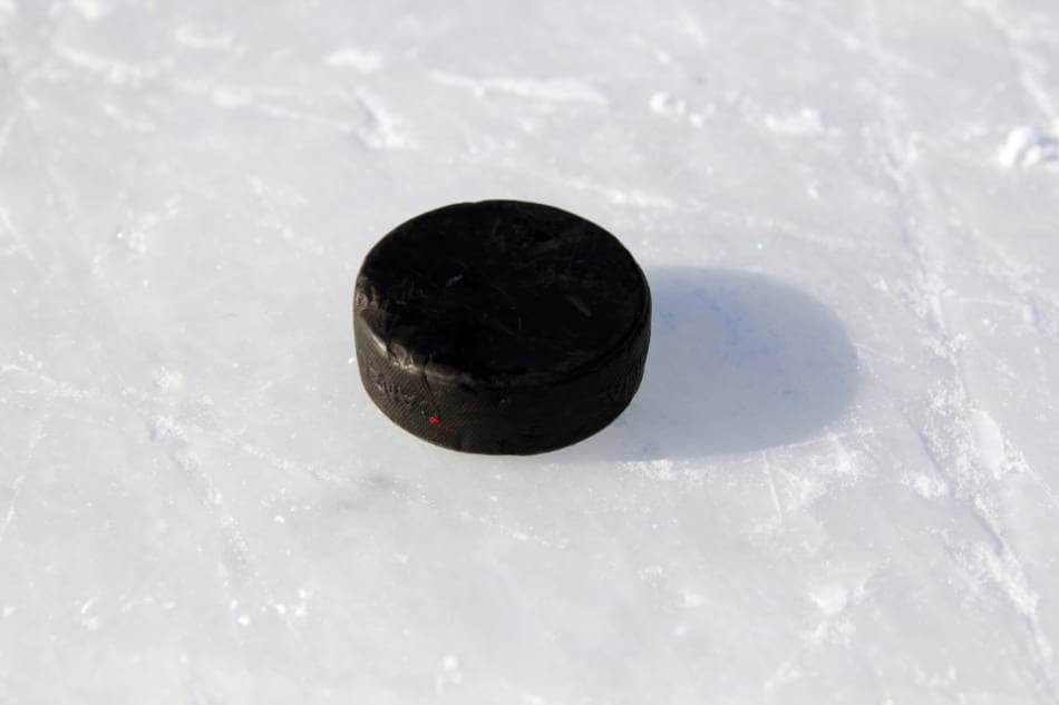 A hockey puck lying on some outdoor ice.