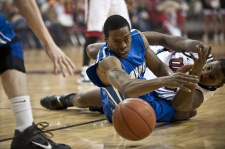 Two college basketball players dive for a loose ball.