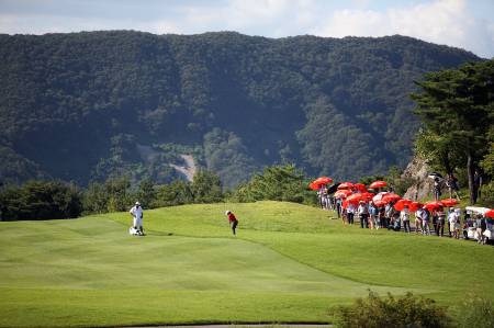 A caddie looks on as his golfer prepares to take a shot.