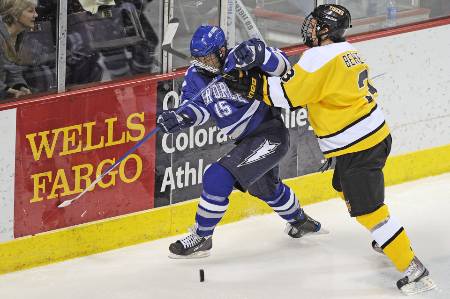 A college hockey player in yellow finishes his check against a player in blue.