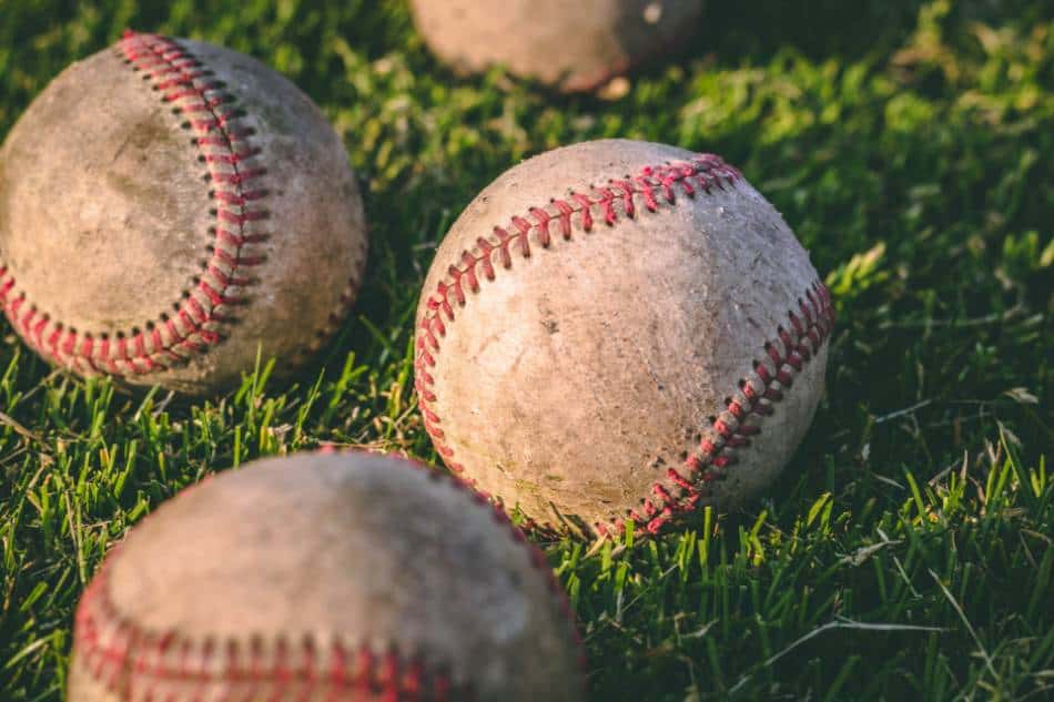 Some beat-up baseballs lying in the grass.