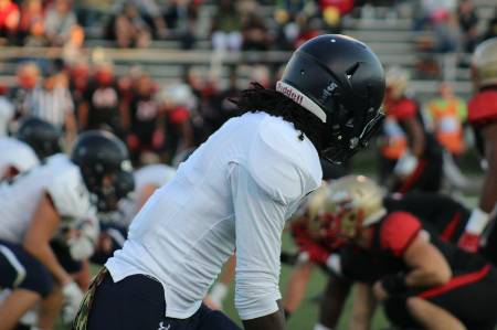 A high school wide receiver looks toward the quarterback as he lines up on the line of scrimmage.