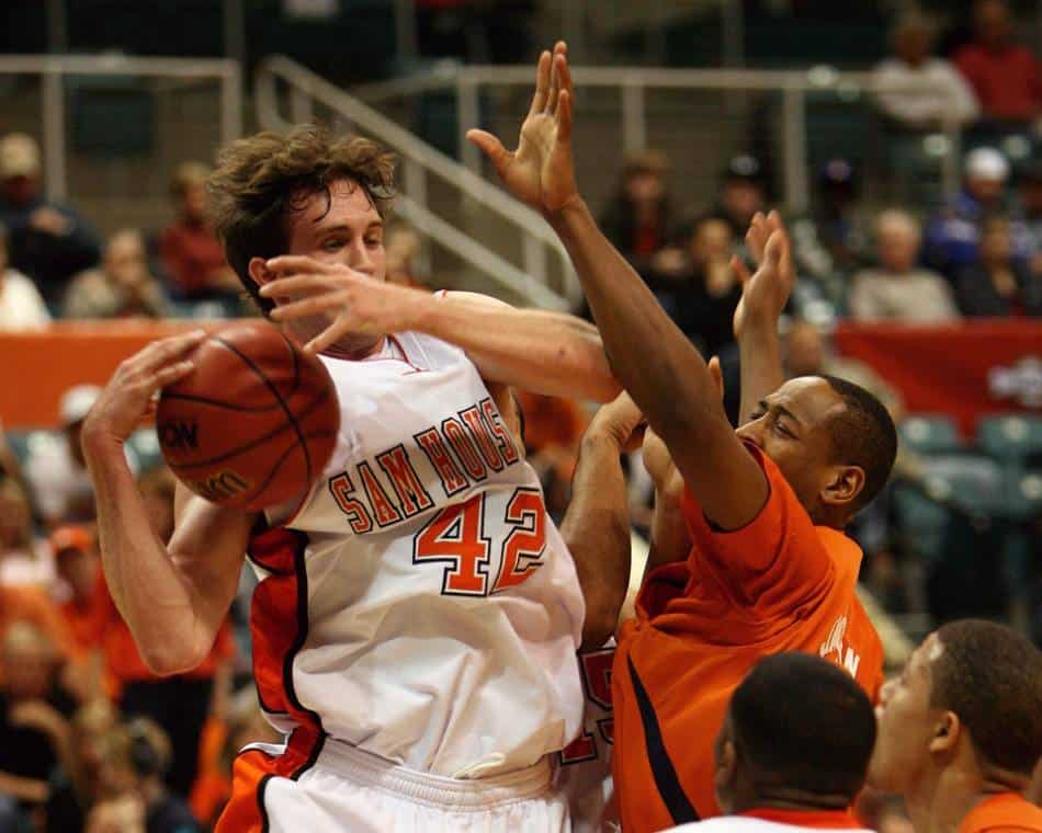 A college basketball player gets fouled as he goes up for a shot.