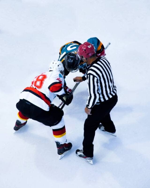 A hockey ref prepares to drop the puck for a faceoff.