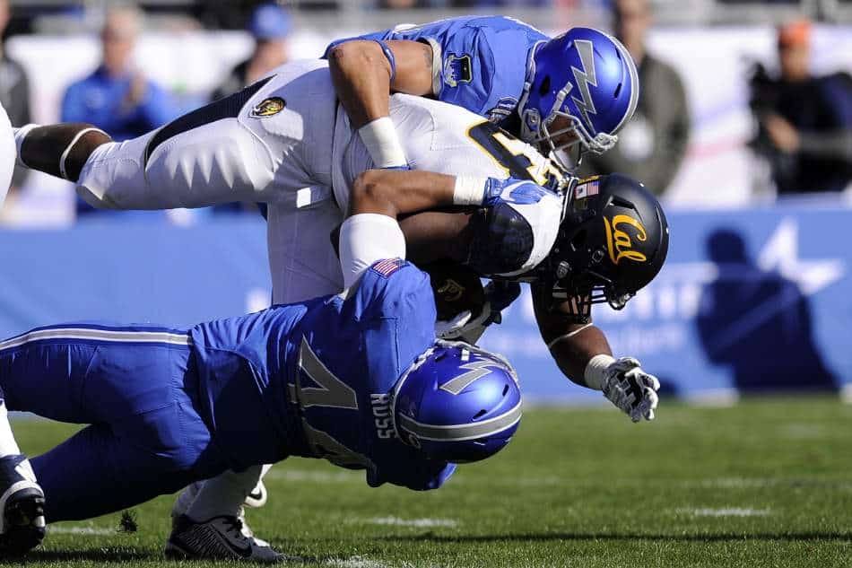 Two college football players in blue tackle a Cal player.